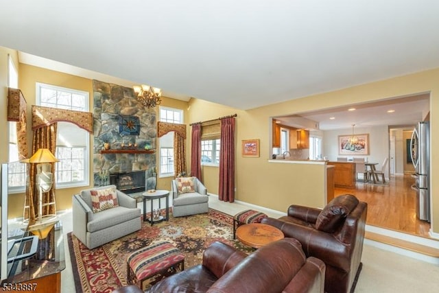 living area with baseboards, a notable chandelier, a stone fireplace, and light wood-style flooring