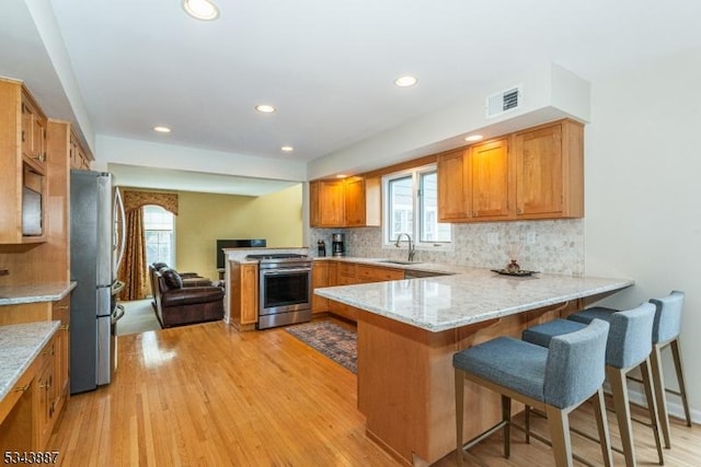 kitchen featuring visible vents, a sink, stainless steel appliances, a peninsula, and light wood finished floors