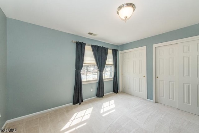 unfurnished bedroom with carpet, baseboards, visible vents, and multiple closets