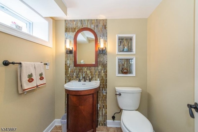 bathroom with vanity, toilet, baseboards, and backsplash