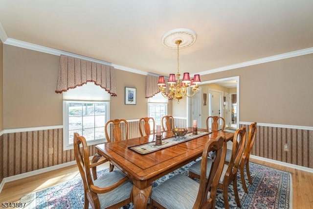 dining area featuring an inviting chandelier, crown molding, light wood finished floors, and wainscoting