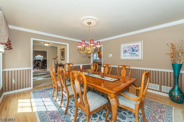 dining area with a wainscoted wall, light wood-style floors, a chandelier, and ornamental molding