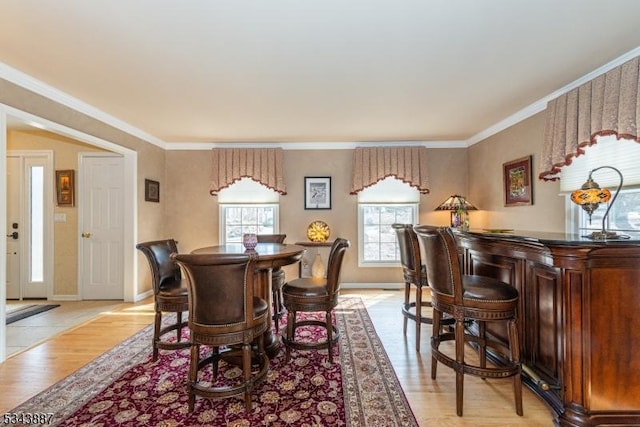 dining room with a bar, crown molding, light wood-style flooring, and baseboards