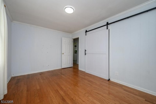 unfurnished bedroom with a barn door, wood finished floors, baseboards, and ornamental molding