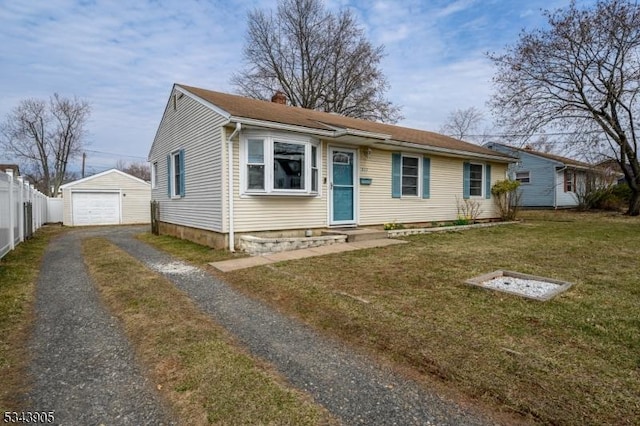 view of front facade with an outbuilding, aphalt driveway, a detached garage, fence, and a front yard