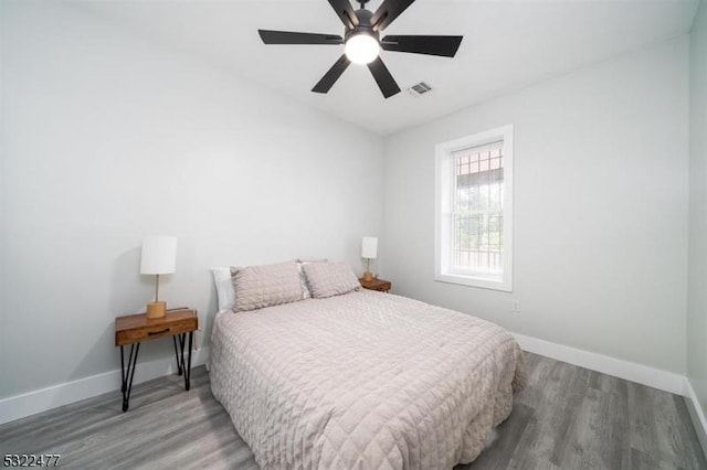 bedroom with a ceiling fan, wood finished floors, visible vents, and baseboards