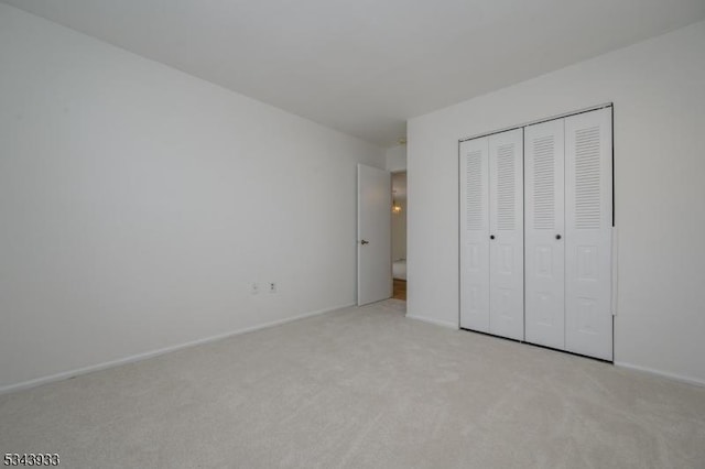 unfurnished bedroom featuring light colored carpet, a closet, and baseboards