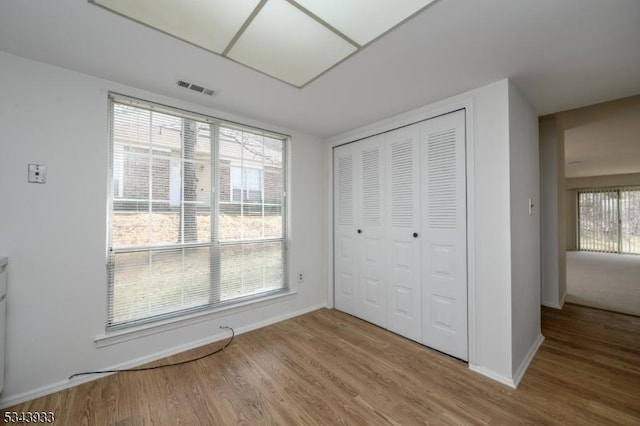 unfurnished bedroom featuring wood finished floors, visible vents, a closet, and baseboards