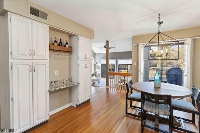 dining area with visible vents, ceiling fan with notable chandelier, light wood-type flooring, and baseboards