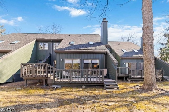 back of house with a deck, a chimney, and a shingled roof