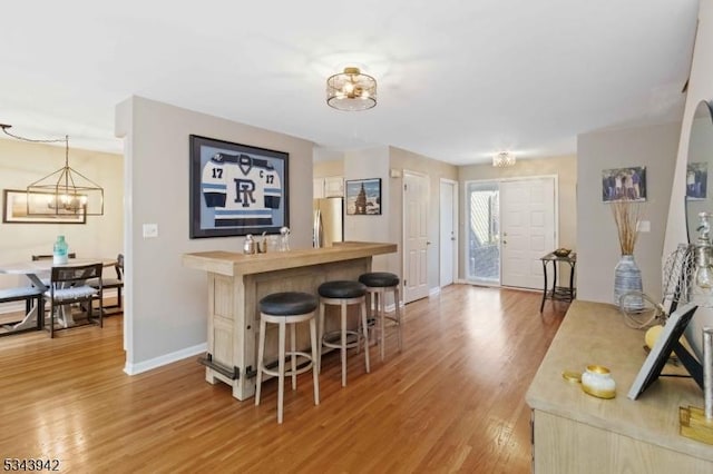 kitchen featuring light wood finished floors, a notable chandelier, a breakfast bar, and freestanding refrigerator