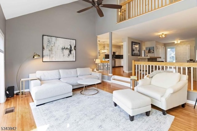 living area with visible vents, baseboards, wood finished floors, high vaulted ceiling, and a ceiling fan