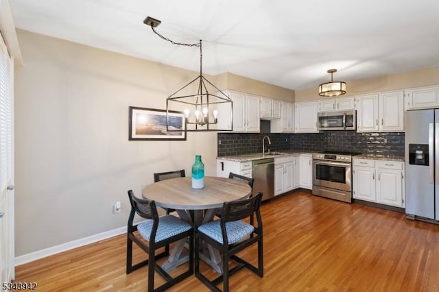 kitchen featuring wood finished floors, baseboards, stainless steel appliances, decorative backsplash, and white cabinets