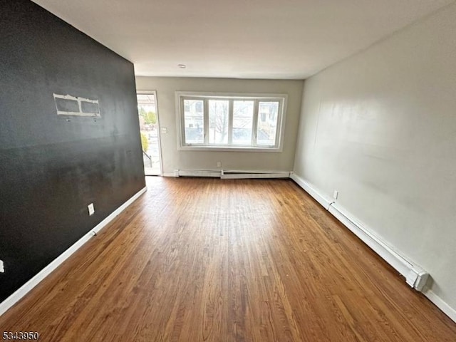 spare room with wood finished floors, baseboards, and baseboard heating