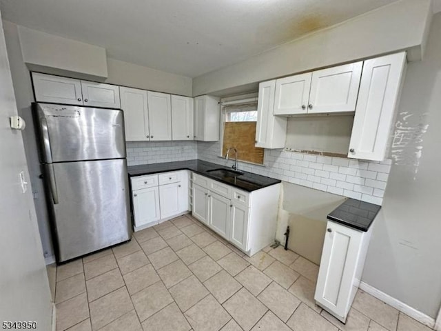 kitchen with a sink, tasteful backsplash, freestanding refrigerator, white cabinets, and baseboards