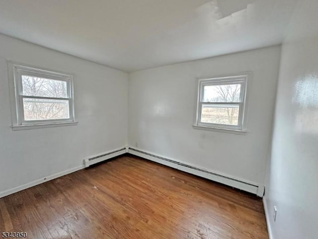 empty room featuring baseboard heating, plenty of natural light, baseboards, and wood finished floors