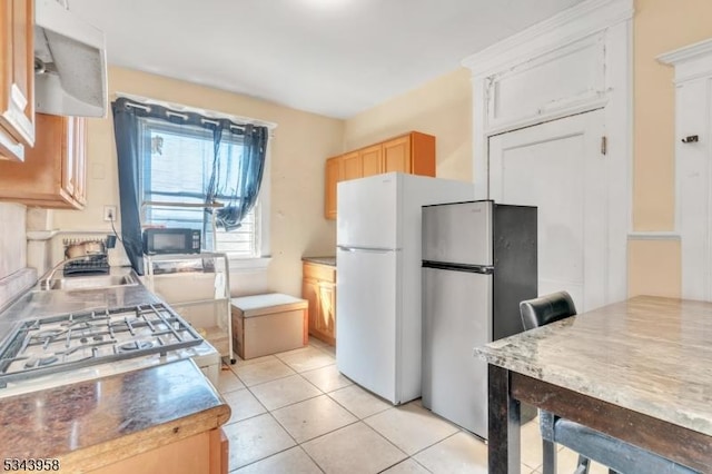 kitchen featuring a sink, freestanding refrigerator, gas stove, black microwave, and light tile patterned floors