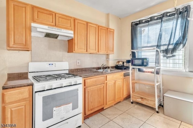 kitchen with light brown cabinetry, a sink, white gas range oven, under cabinet range hood, and dark countertops