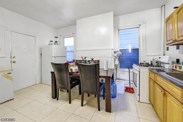 kitchen with dark countertops, decorative backsplash, light tile patterned flooring, white appliances, and a sink