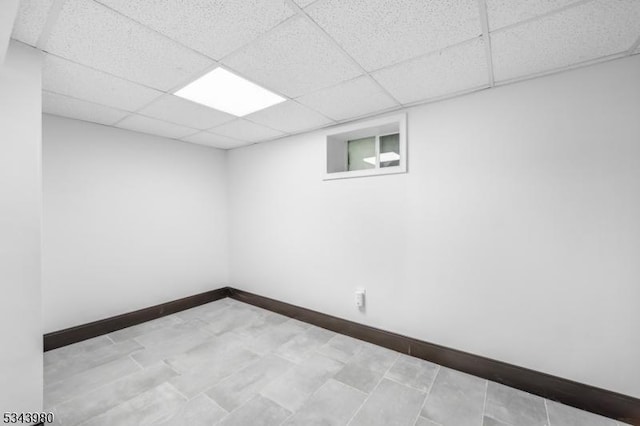 finished basement featuring a paneled ceiling and baseboards