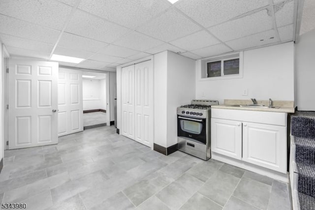 kitchen with stainless steel gas stove, a sink, white cabinets, light countertops, and a paneled ceiling