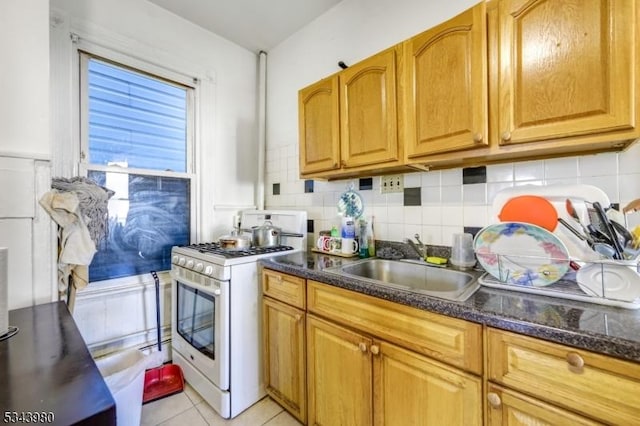 kitchen with decorative backsplash, white range with gas cooktop, light tile patterned floors, and a sink