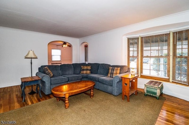 living area featuring arched walkways, a healthy amount of sunlight, crown molding, and wood finished floors