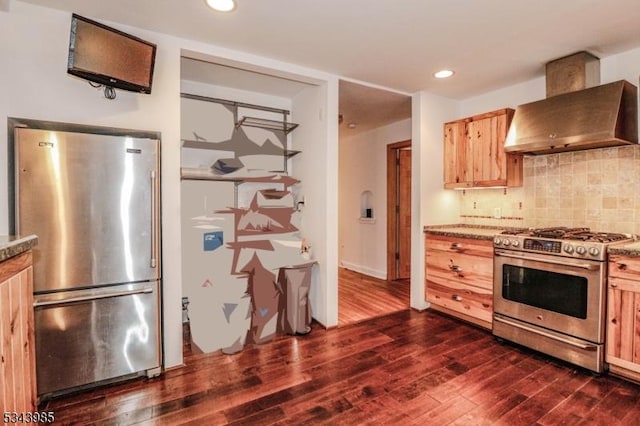 kitchen featuring dark wood finished floors, light brown cabinetry, decorative backsplash, appliances with stainless steel finishes, and wall chimney range hood