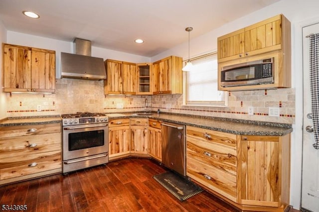 kitchen featuring a sink, dark countertops, dark wood finished floors, stainless steel appliances, and wall chimney exhaust hood