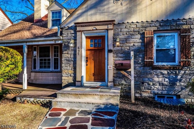 view of exterior entry featuring stone siding, roof with shingles, and a chimney