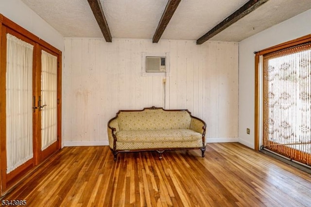 unfurnished room with beamed ceiling, french doors, a wall unit AC, and hardwood / wood-style floors