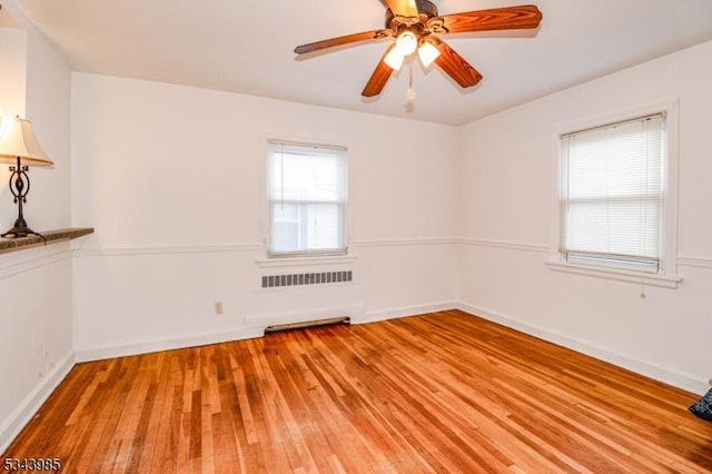 empty room featuring radiator heating unit, baseboards, light wood-type flooring, and ceiling fan