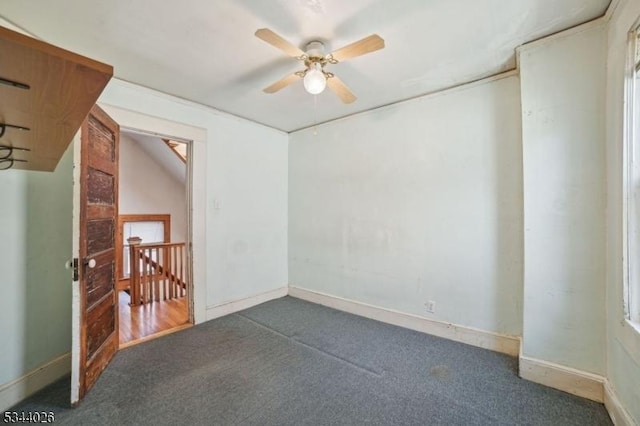 empty room with dark colored carpet, baseboards, and a ceiling fan