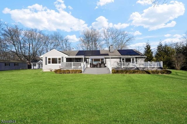 back of property featuring a deck, solar panels, a chimney, and a yard