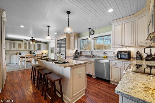 kitchen with a kitchen island, appliances with stainless steel finishes, a kitchen breakfast bar, dark wood-style floors, and a sink