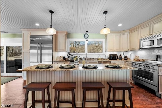 kitchen featuring light stone counters, cream cabinetry, backsplash, and high quality appliances