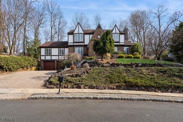 tudor-style house featuring decorative driveway, an attached garage, and stucco siding