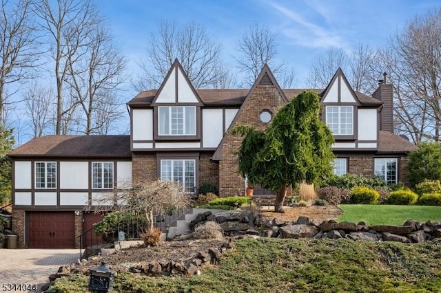 english style home with brick siding, a garage, driveway, and a chimney