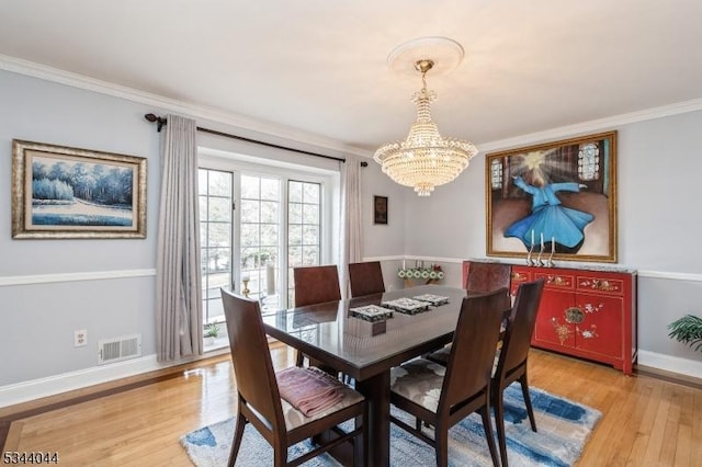 dining space featuring light wood finished floors, visible vents, crown molding, baseboards, and a notable chandelier