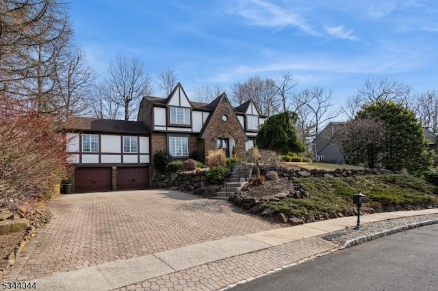 english style home with brick siding, stucco siding, an attached garage, and decorative driveway