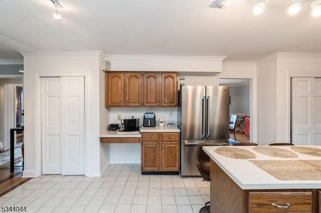 kitchen featuring light tile patterned floors, light countertops, brown cabinetry, and freestanding refrigerator