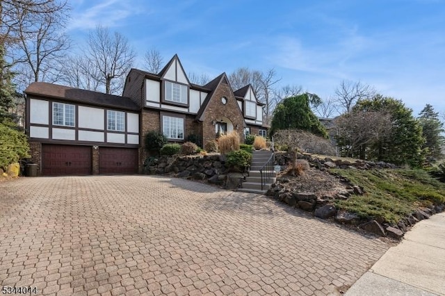 english style home featuring an attached garage, brick siding, driveway, and stucco siding