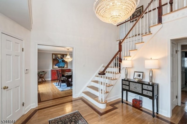 stairway with baseboards, a notable chandelier, a high ceiling, and wood finished floors