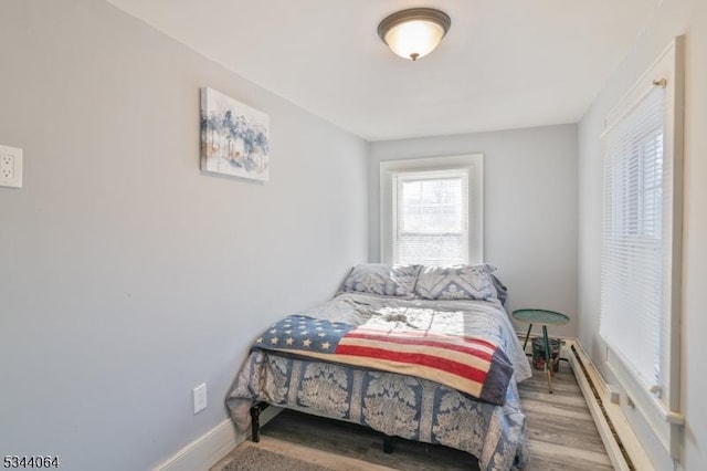 bedroom featuring a baseboard heating unit, wood finished floors, and baseboards