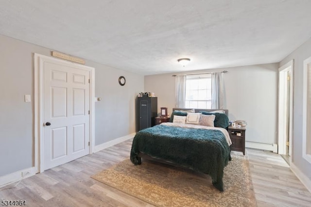 bedroom featuring a baseboard heating unit, baseboards, and light wood-style flooring