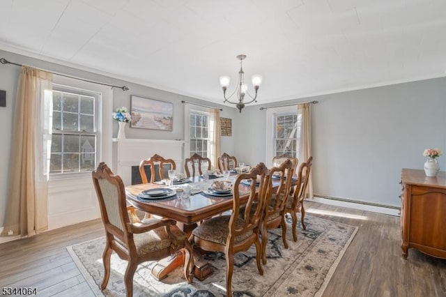 dining space with an inviting chandelier, crown molding, wood finished floors, and baseboard heating