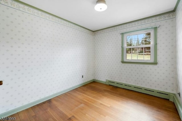 spare room with light wood-type flooring, ornamental molding, wallpapered walls, a baseboard radiator, and baseboards