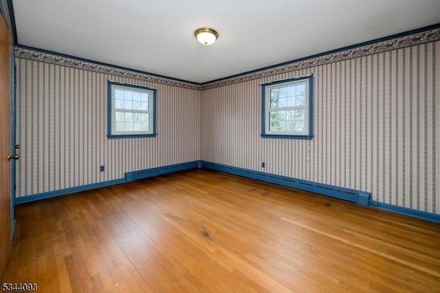 empty room with baseboards, wood-type flooring, a healthy amount of sunlight, and wallpapered walls