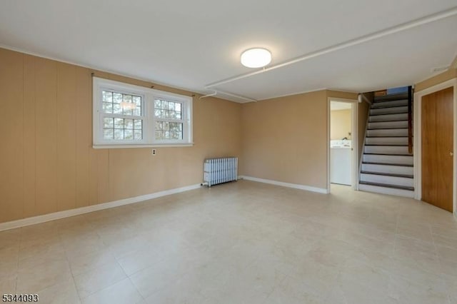 spare room featuring wooden walls, baseboards, stairway, radiator heating unit, and washer / dryer