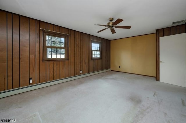 unfurnished room with visible vents, wood walls, light colored carpet, baseboard heating, and a ceiling fan